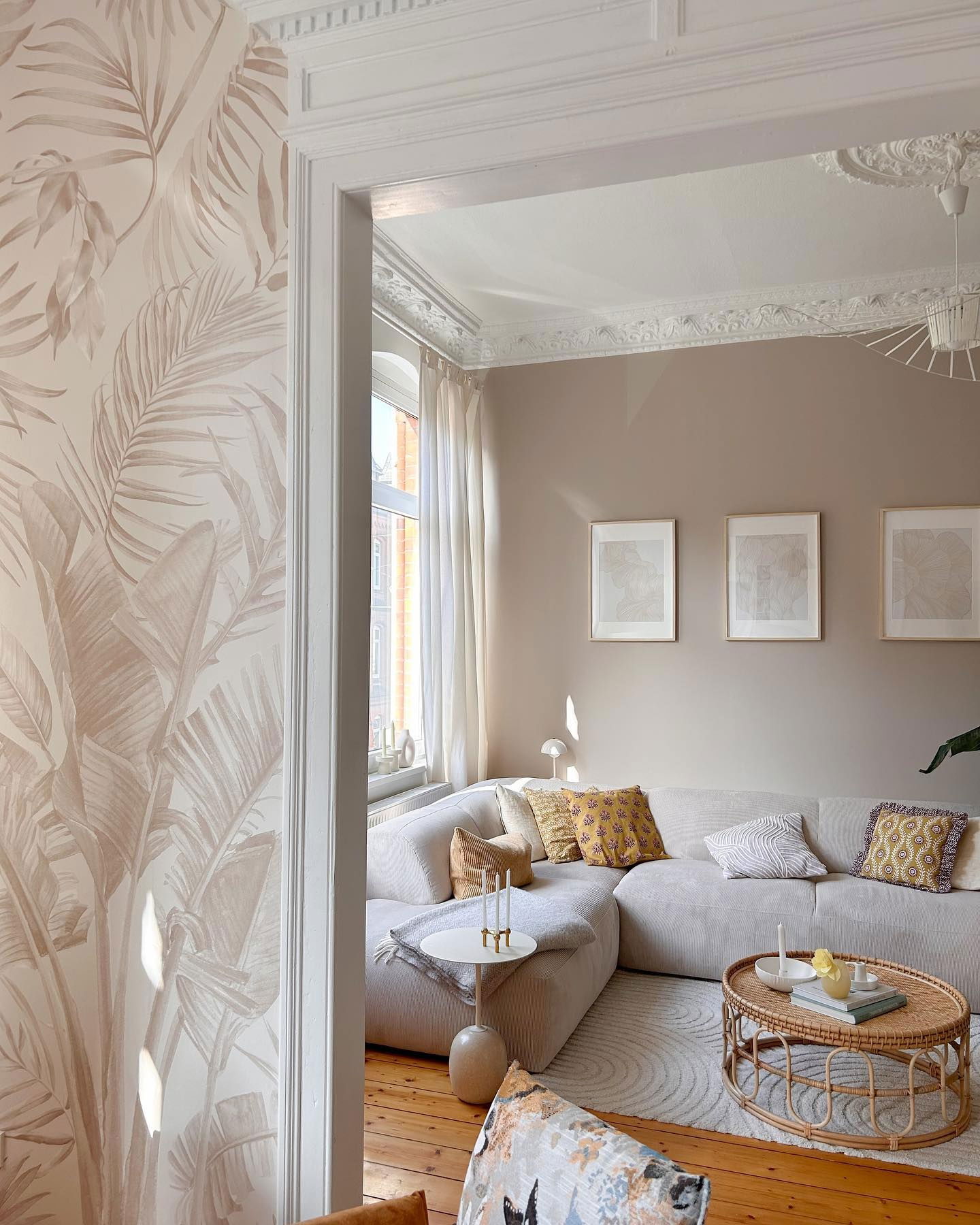 Living room with beige sectional sofa, rattan coffee table, and tropical leaf wallpaper.