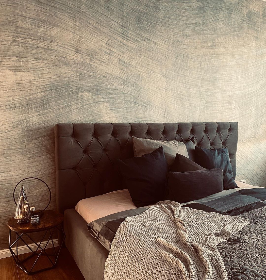 Bedroom with gray tufted headboard, throw pillows, and knit blanket. Nightstand with decorative lamp.