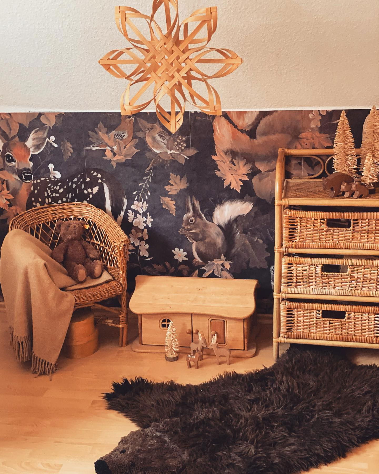 Chambre confortable avec papier peint à motifs de forêt, meubles en osier et tapis en peau d'ours.