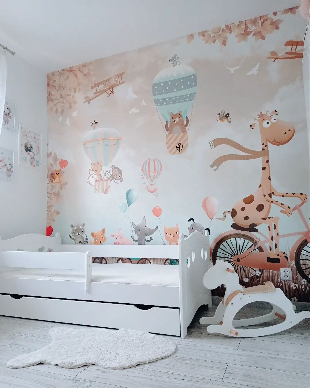 Child's room with white bed, rocking horse, and whimsical wallpaper featuring animals, balloons, and airplanes.