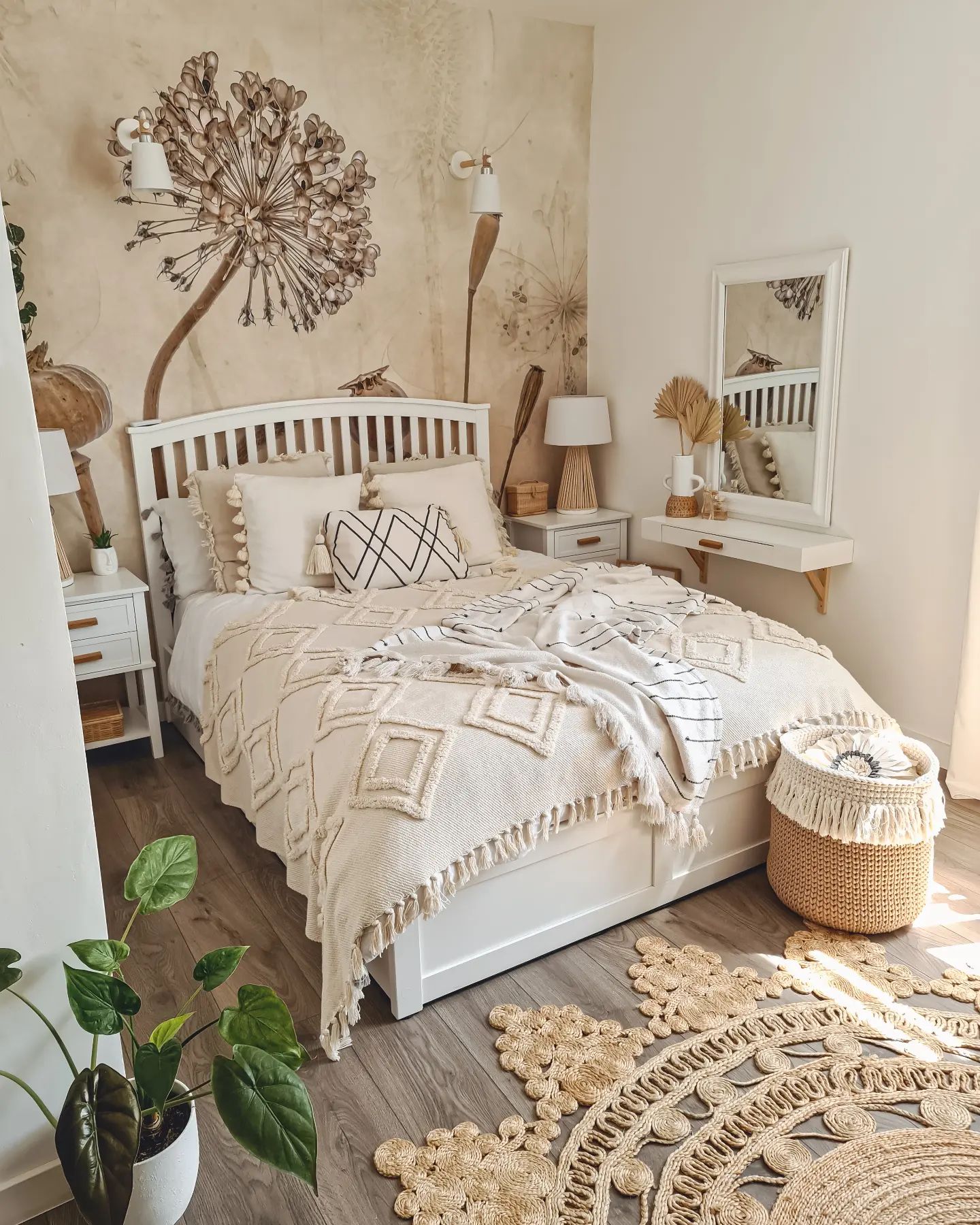 Chambre confortable avec lit blanc, literie neutre et décoration murale florale. Un tapis de jute et un panier tissé ajoutent de la texture.
