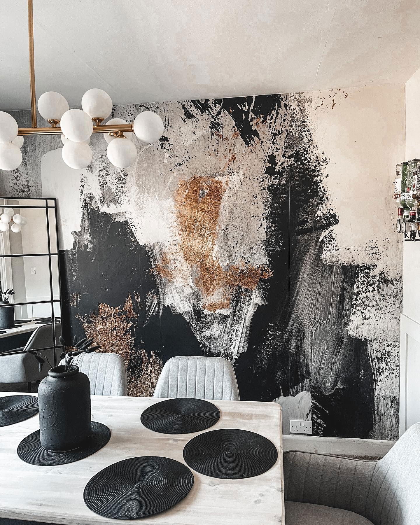 Dining room with abstract black, white, and gold wallpaper. Table is set with black placemats and a black vase.