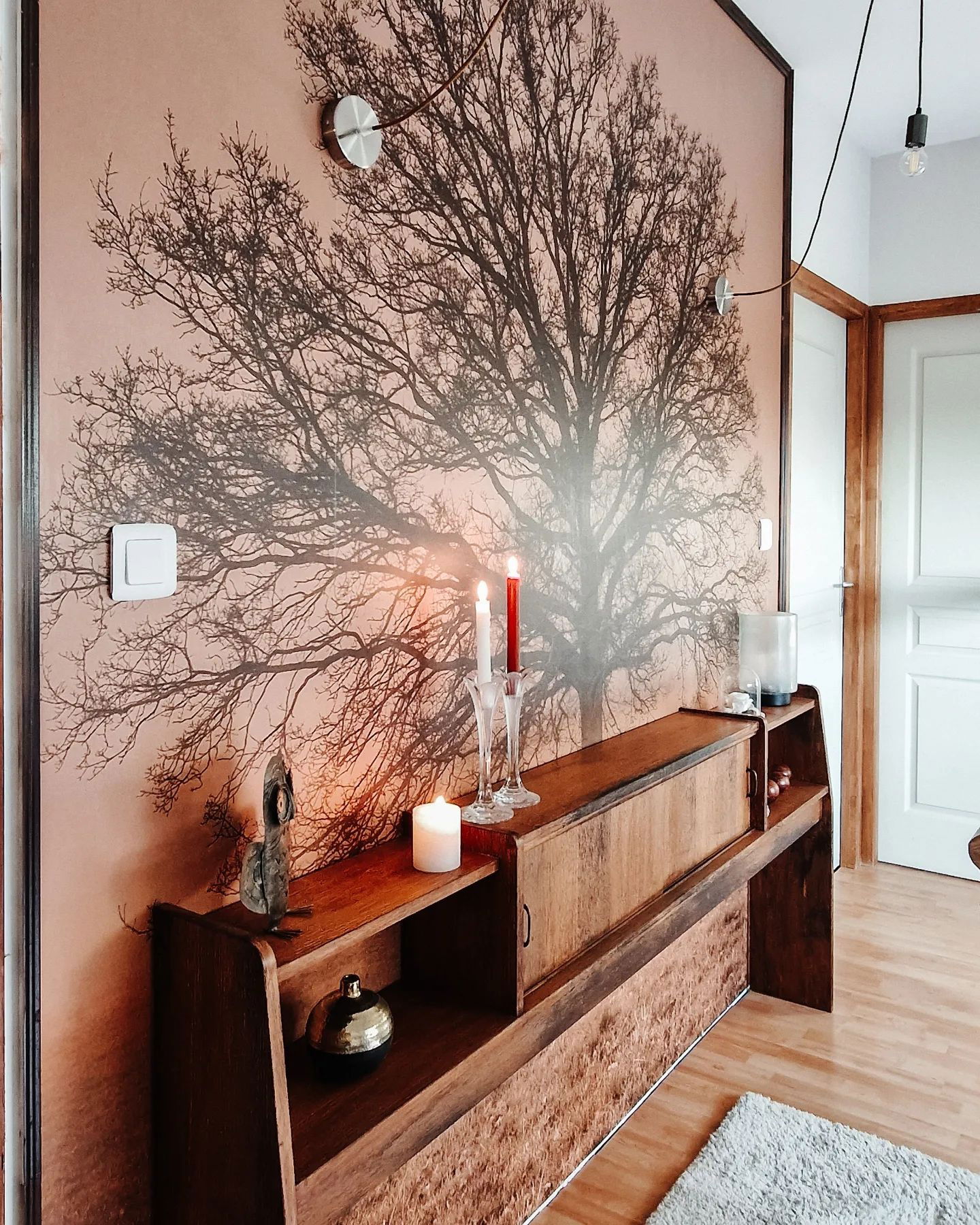 Interieur van een woonkamer met een muurschildering van een boom, een houten kast en brandende kaarsen.