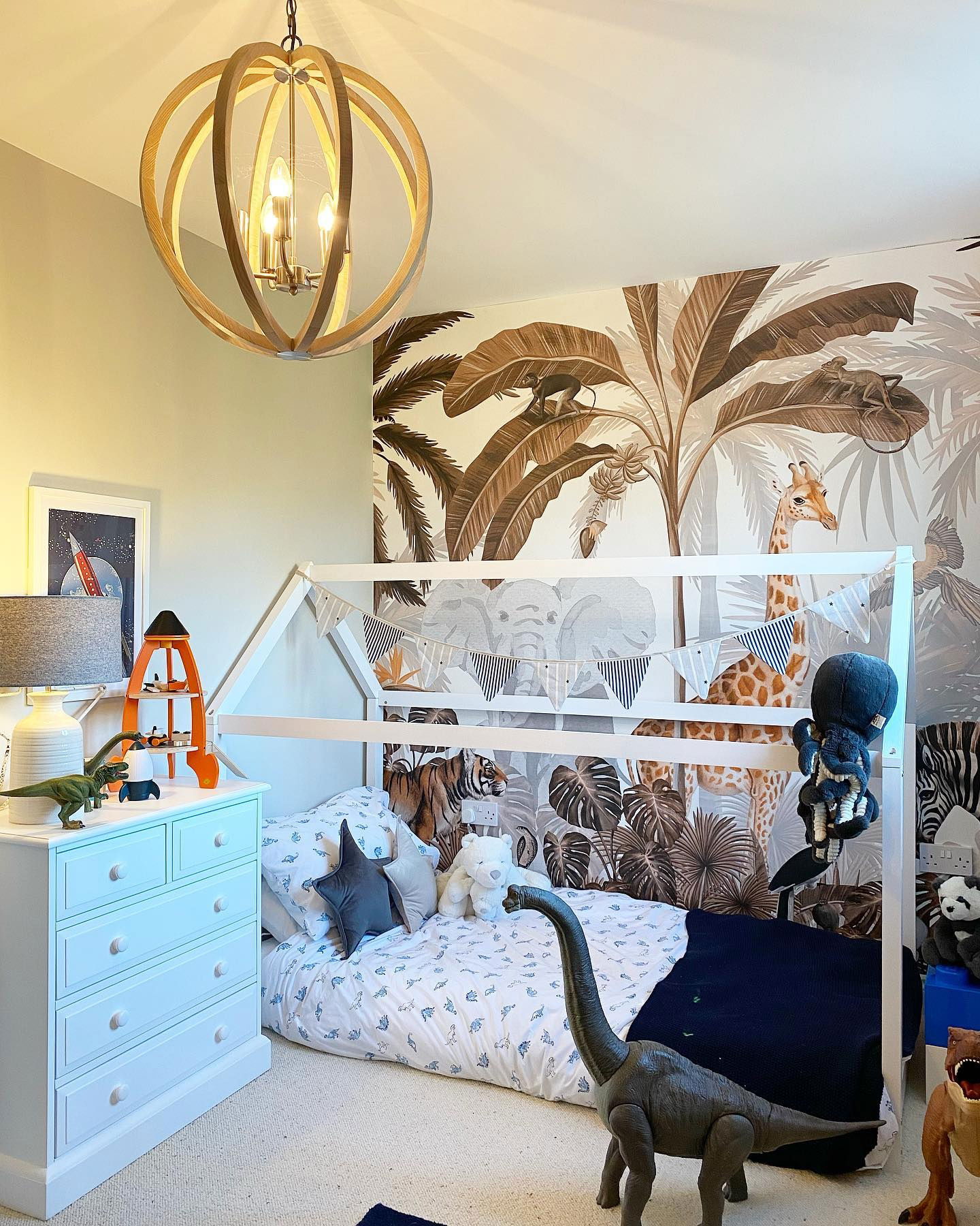 Kinderkamer met junglebehang, wit huisframe bed en houten bolvormige kroonluchter.