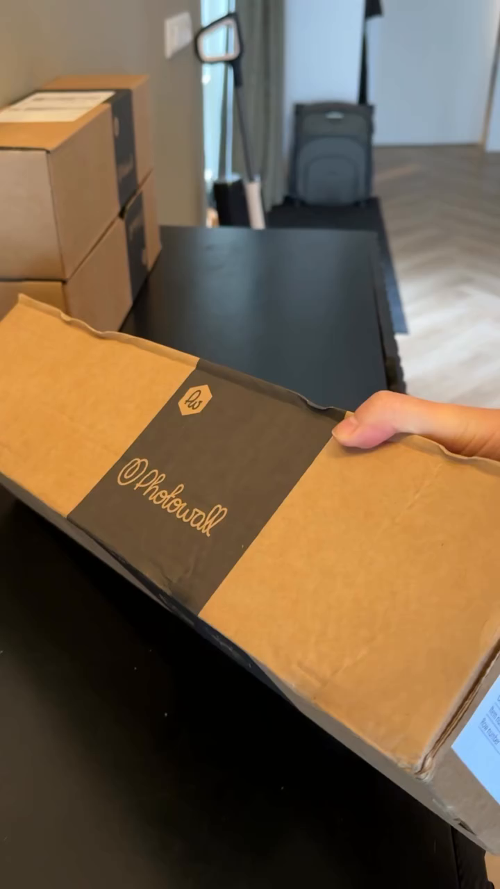 Hand holding a Photowall cardboard box with a black label.