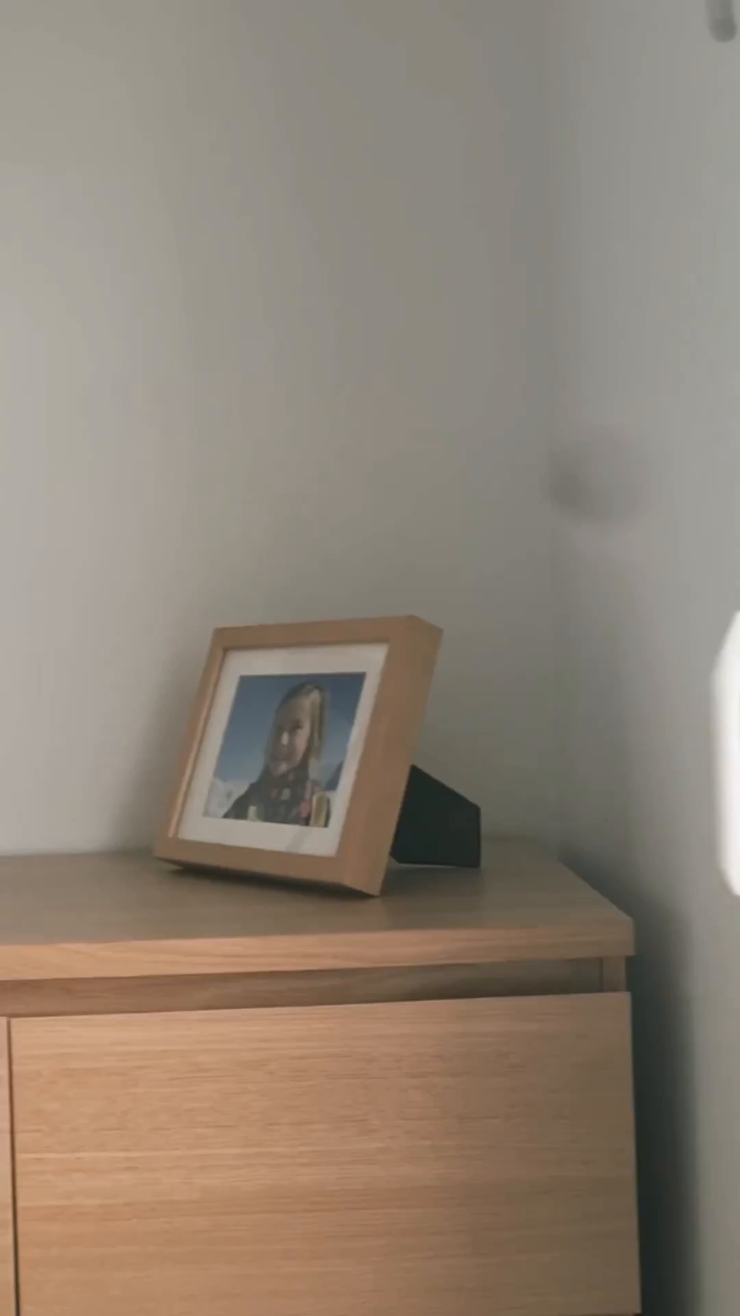 Framed portrait of a child on a light wood dresser against a white wall.