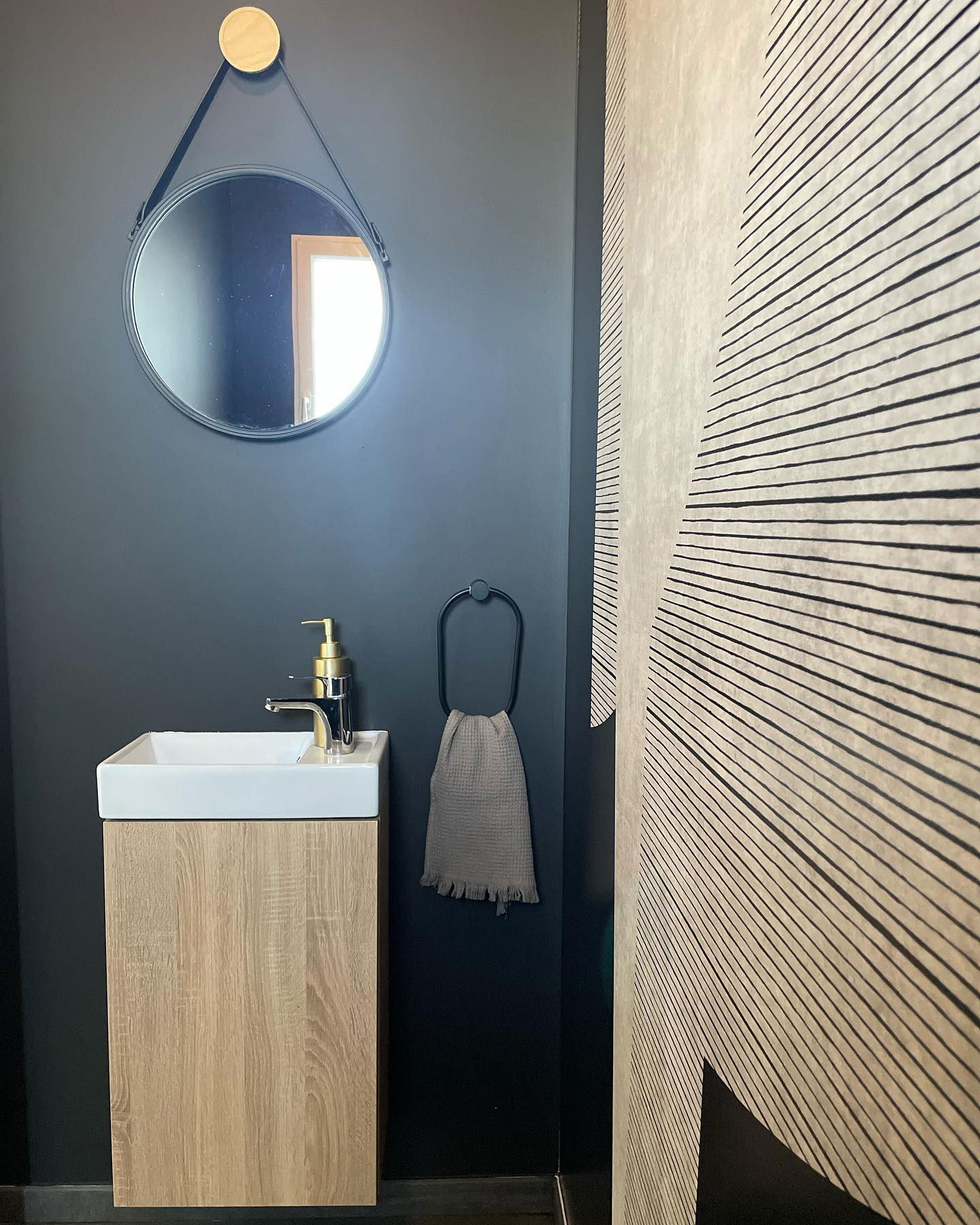 Modern powder room with round mirror, wood vanity, and geometric wallpaper.