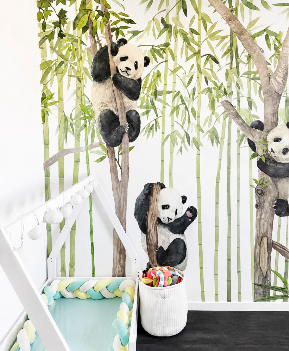 Watercolor pandas climb bamboo trees in a nursery with a white crib and a toy basket.