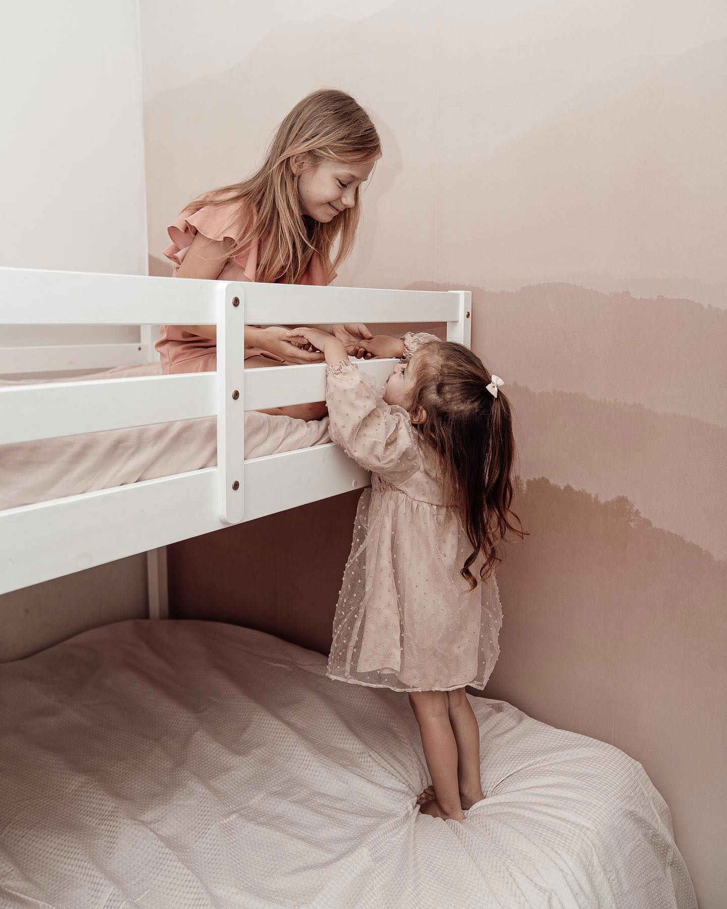 Twee jonge meisjes in roze jurken spelen op een wit stapelbed.
