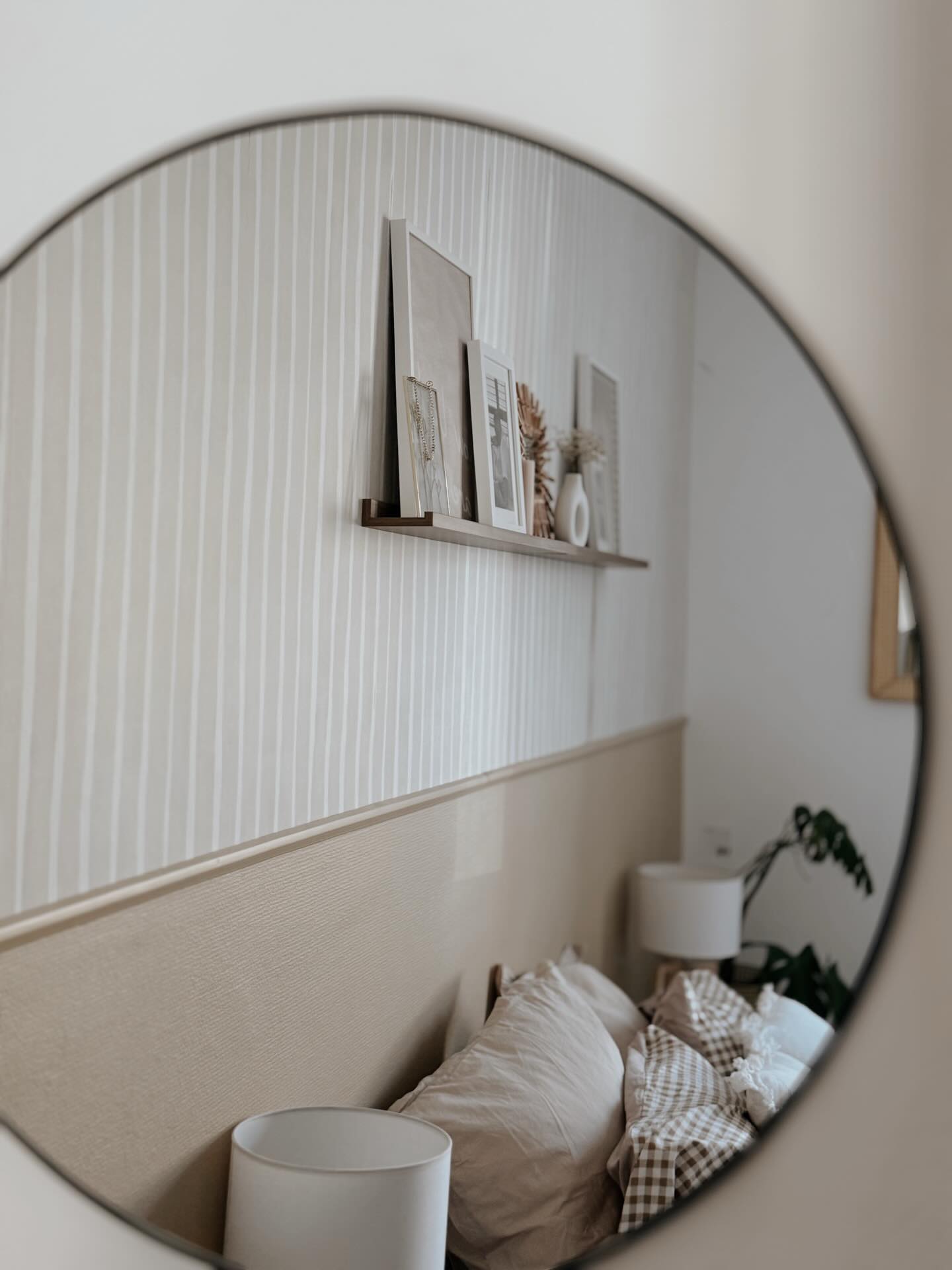 Spiegelung in einem runden Spiegel eines Schlafzimmers mit gerahmter Kunst auf einem Regal über dem Bett.