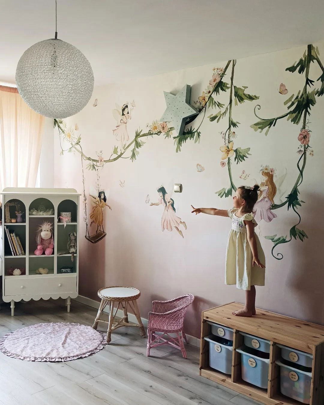 Child in fairy-themed room with wall decals of fairies and vines.