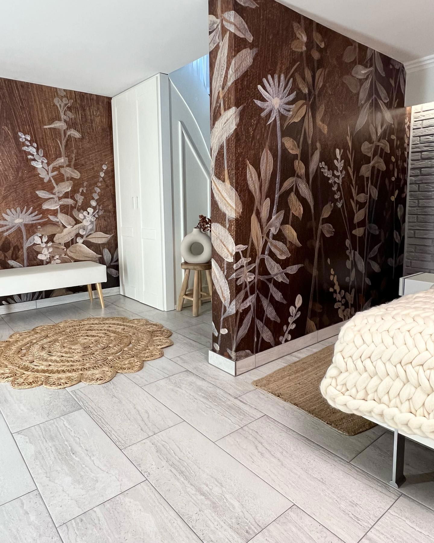 Bedroom interior with floral wallpaper, woven rug, and white furniture.