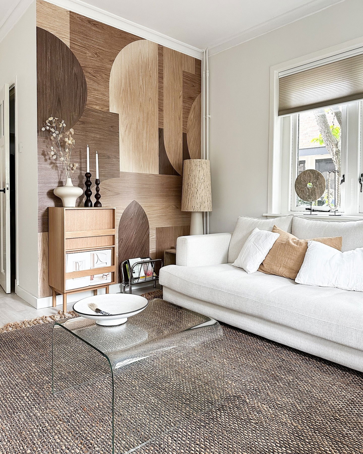 Living room with geometric wood wall art, white sofa, and glass coffee table.