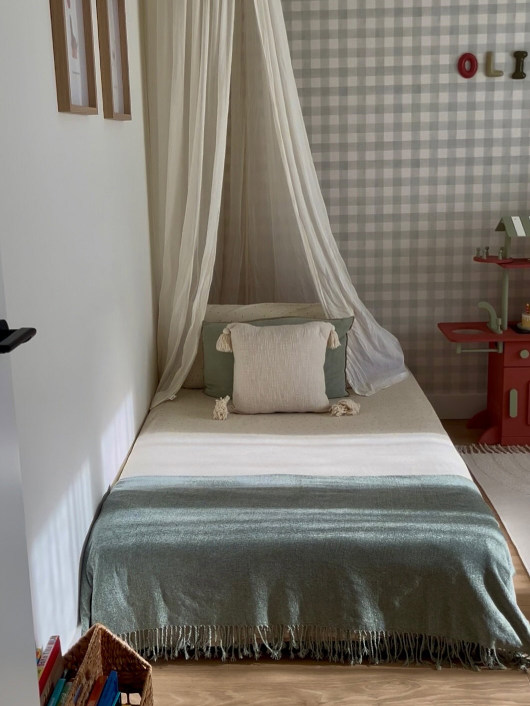 Child's bed with a canopy, white and green bedding, and checkered wallpaper.