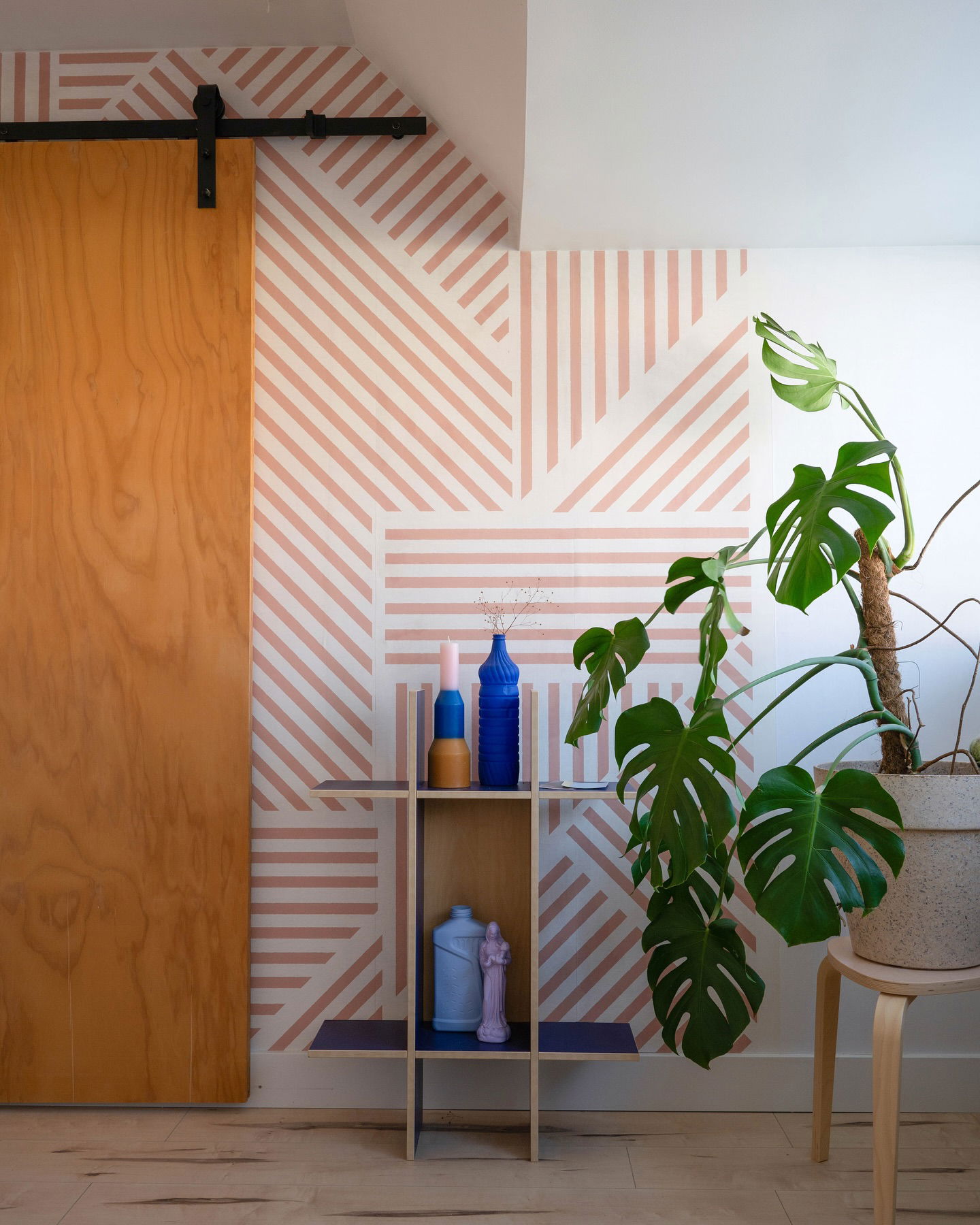 Interior with pink striped wallpaper, wood sliding door, and monstera plant.