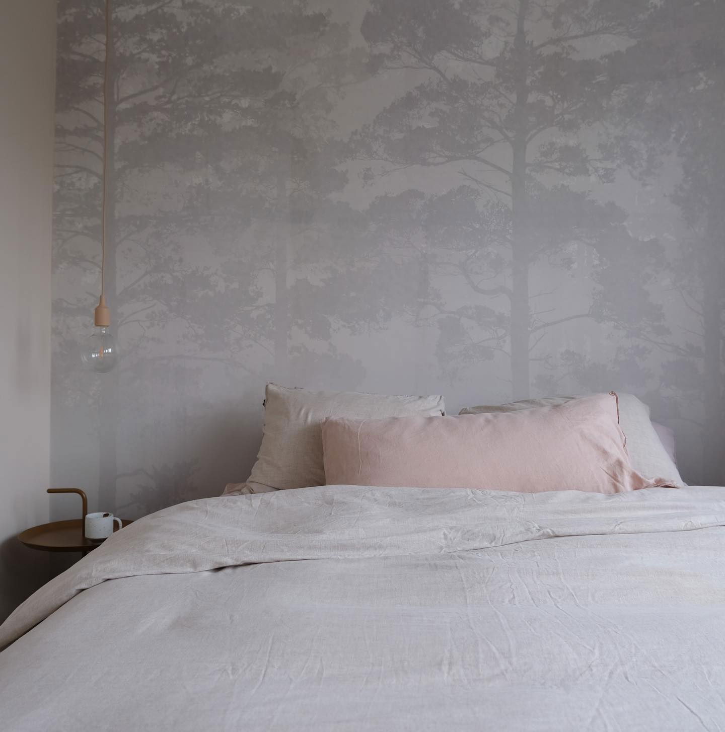 Bedroom with linen bedding, pink lumbar pillow, and forest-themed wallpaper.