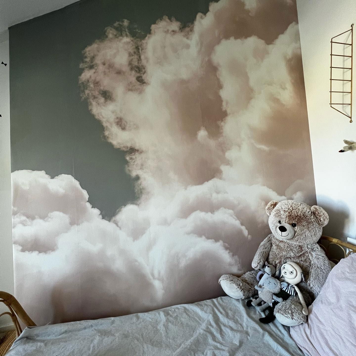 Bedroom with cloud wallpaper, bed with striped bedding, and stuffed animals.