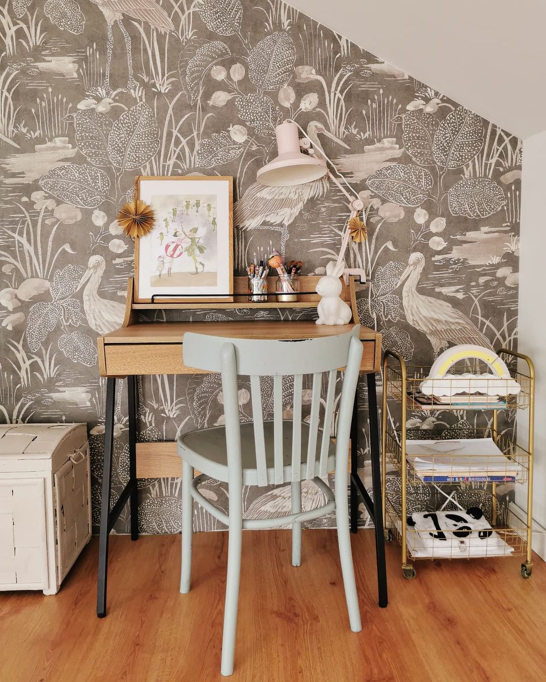 Child's desk area with gray heron wallpaper, light wood desk, and light blue chair.