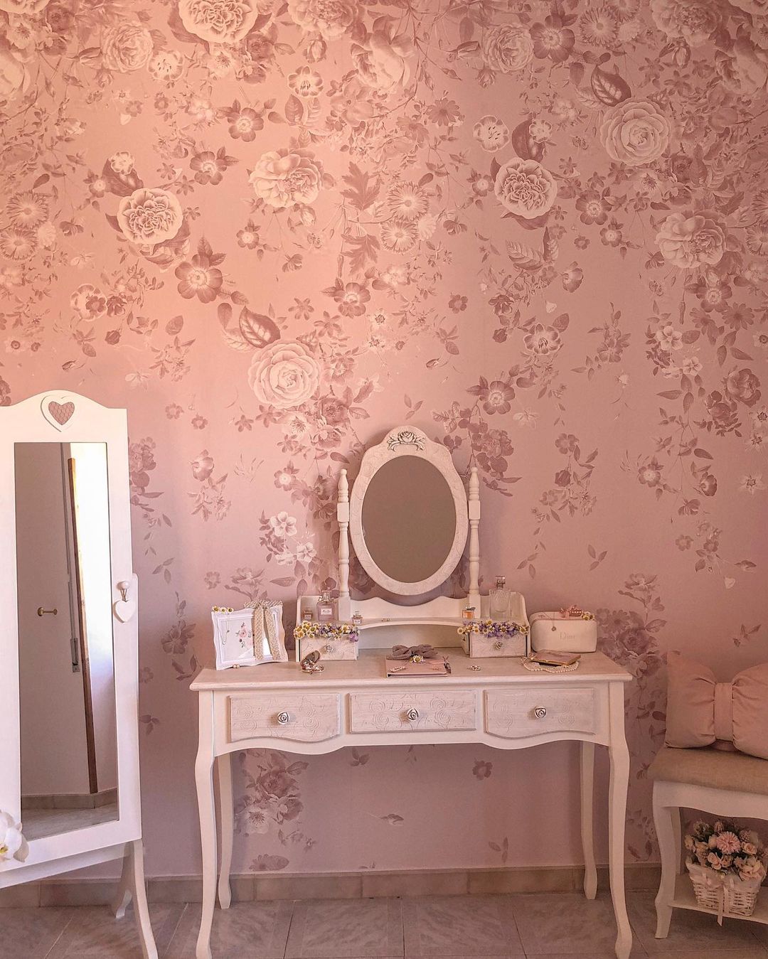 Roze kamer met bloemenbehang, witte wastafel, spiegel en stoel.