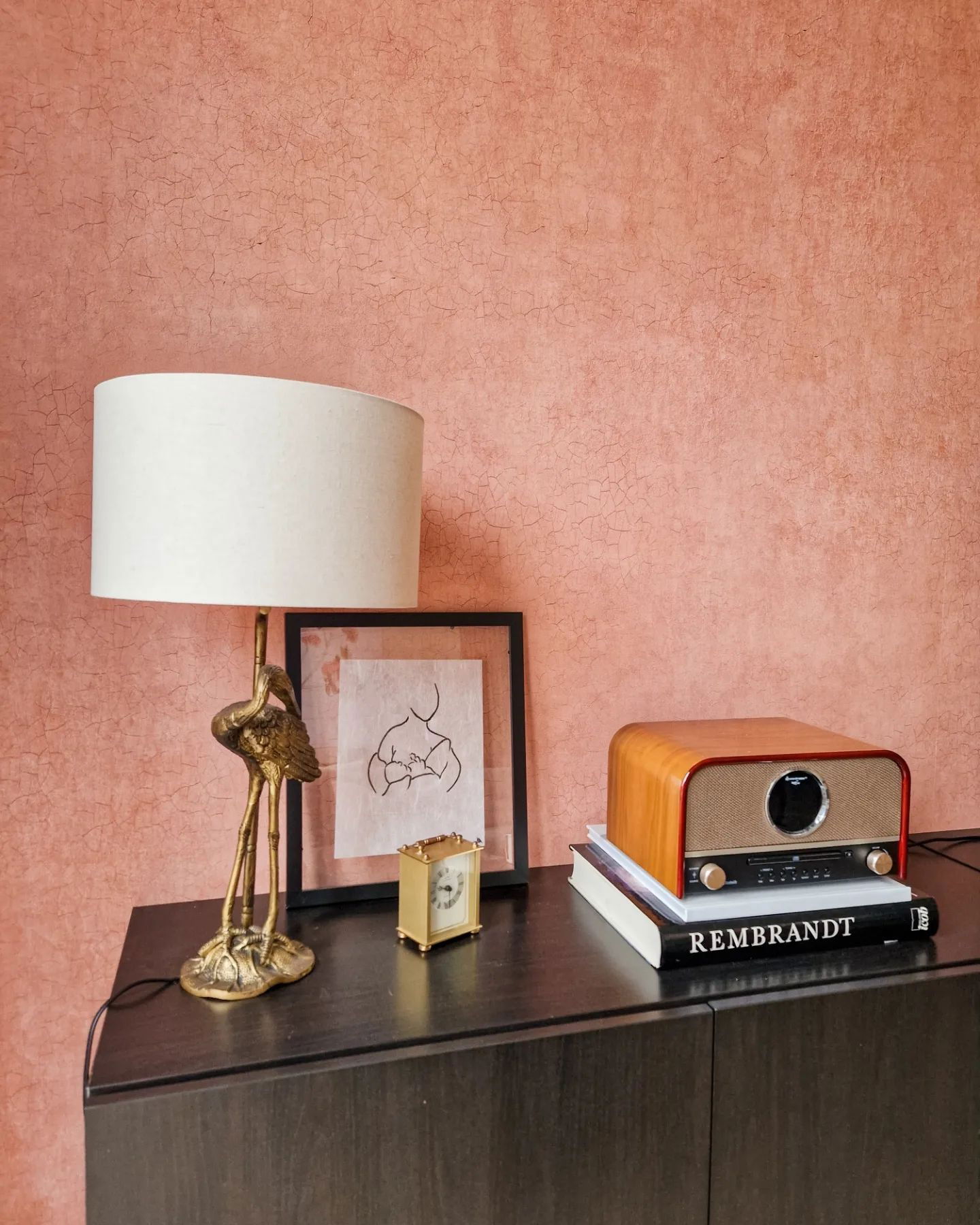 Armoire foncée avec lampe, horloge, œuvre d'art encadrée et radio en bois sur des livres.