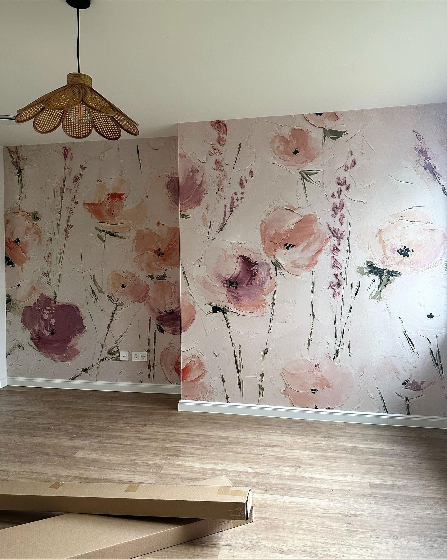 Zimmer mit floraler Tapete, Holzböden und einer Pendelleuchte aus Rattan.