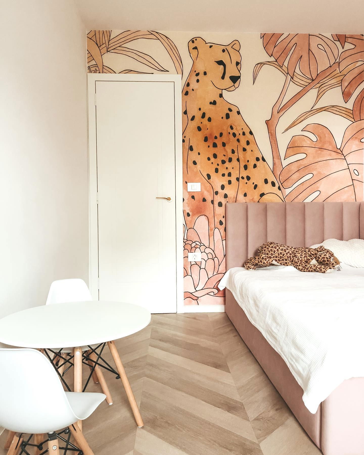 Bedroom with cheetah mural, pink bed, and white table with chairs.