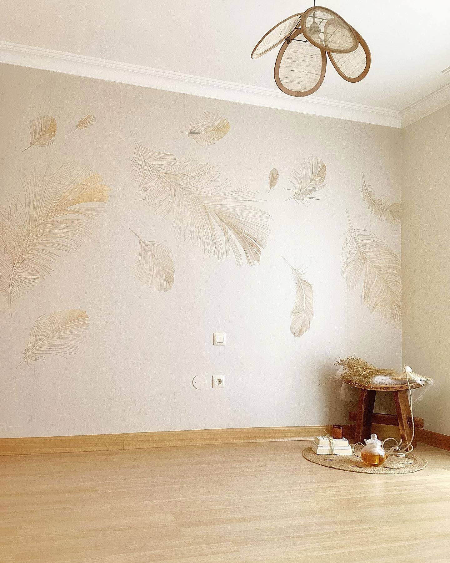 Beige room with feather wall decals, wooden stool, and woven light fixture.