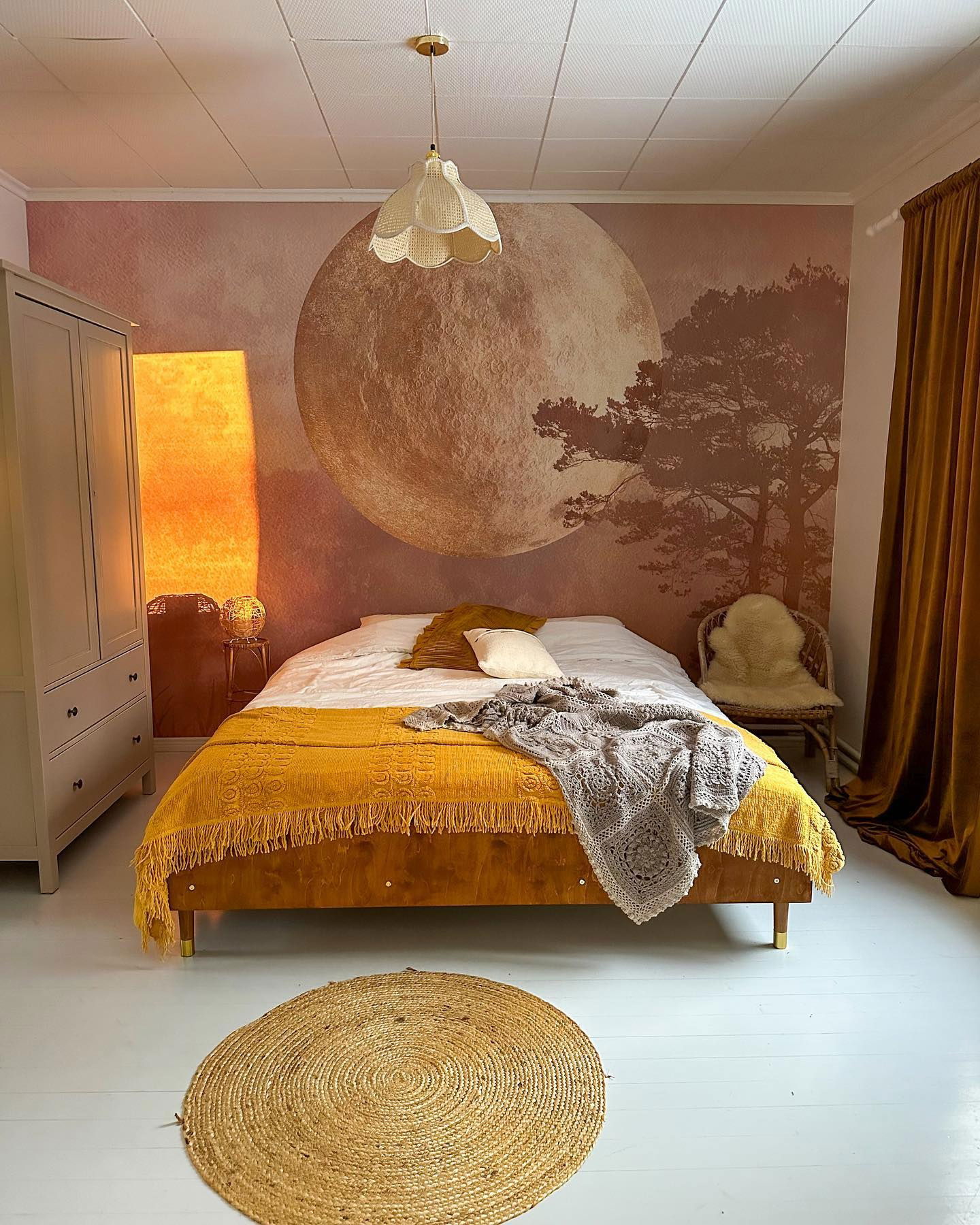 Schlafzimmer mit Mondbild, gelber Tagesdecke und rundem Jute-Teppich.