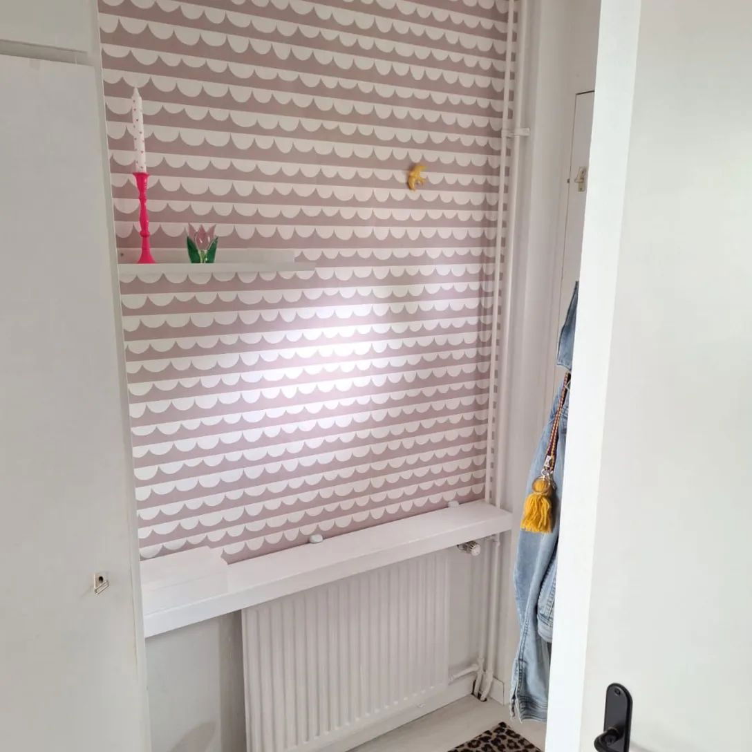 Small nook with patterned wallpaper, white radiator, and shelf.