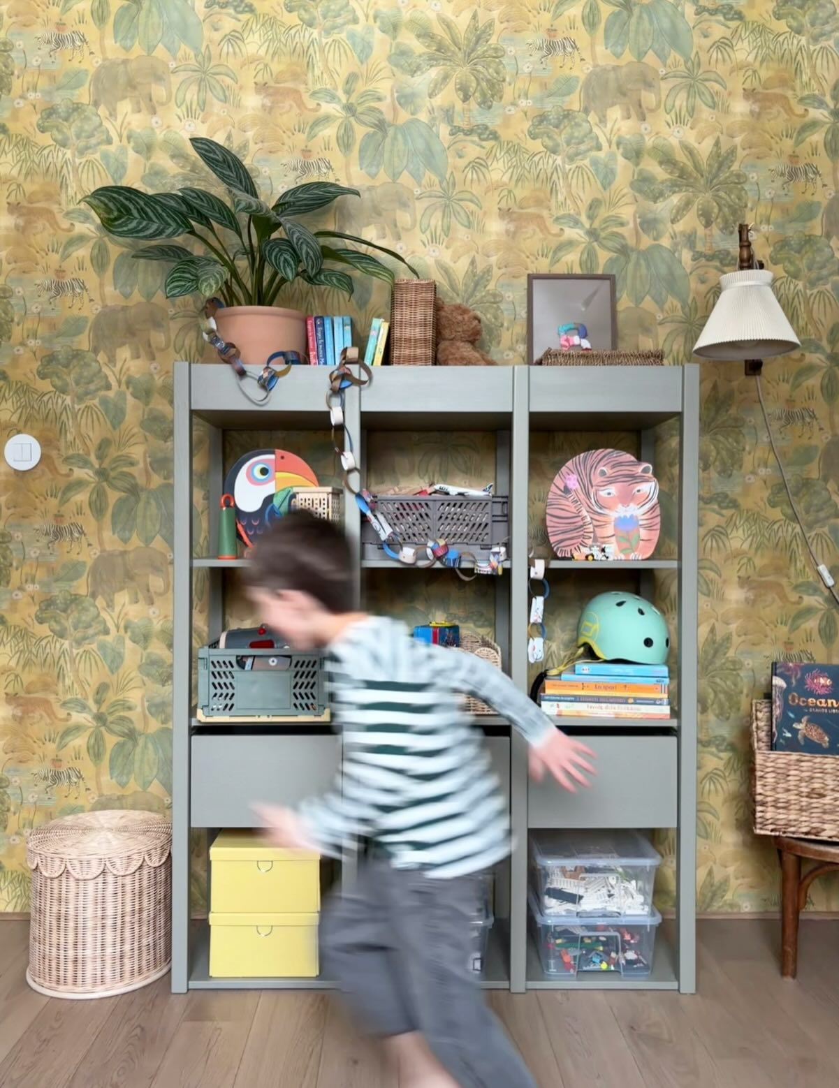 Blurred view of child running past gray bookshelf filled with toys and decorations.