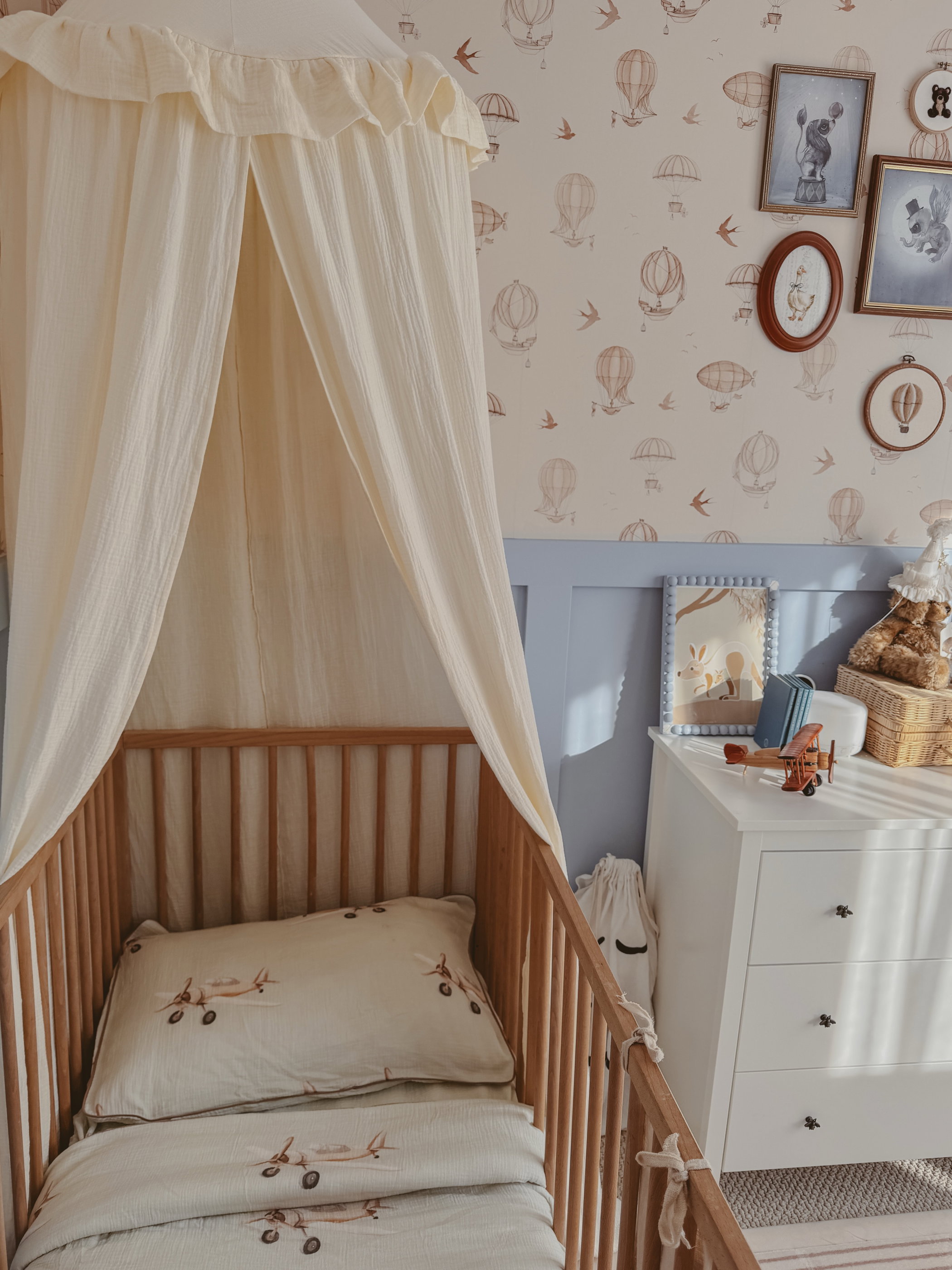 Chambre d'enfant avec berceau, literie d'avion et papier peint montgolfière.