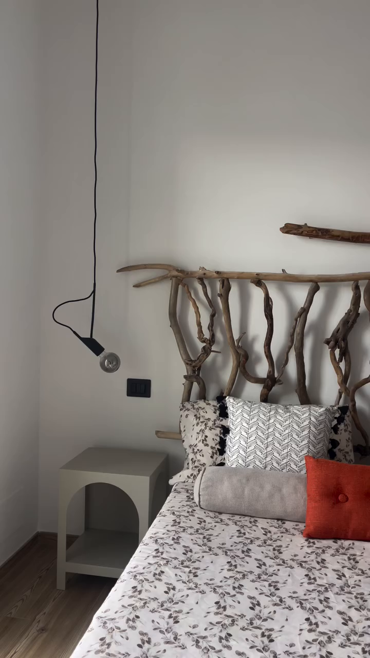 Bedroom with driftwood headboard, floral bedding, and hanging light.