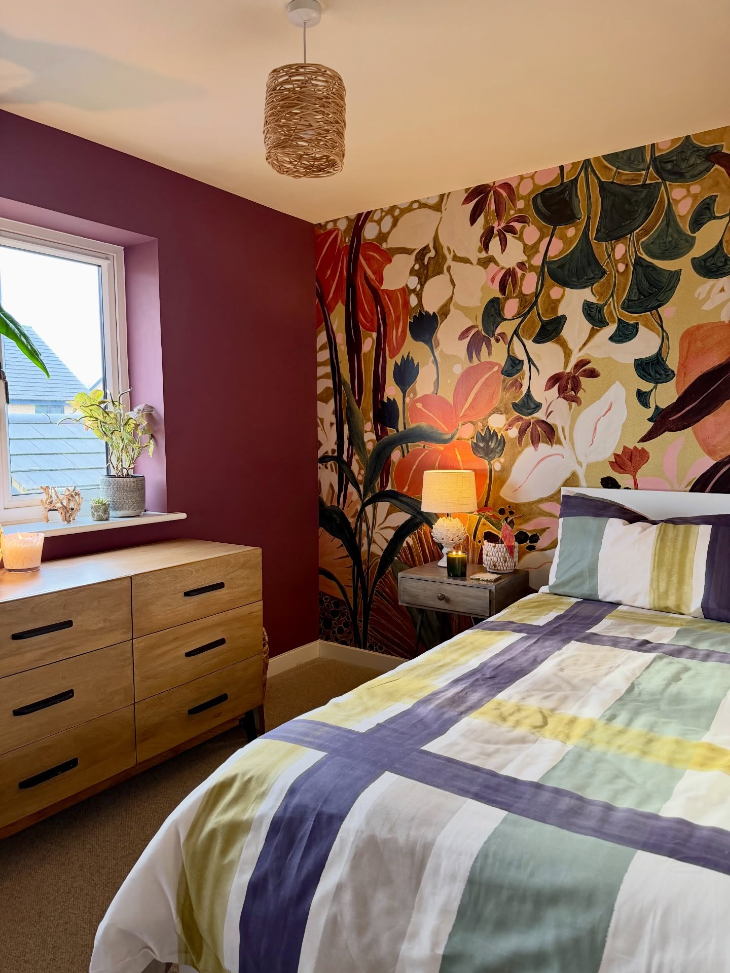 Schlafzimmer mit einer botanischen Wandtapete, einer Holzkommode und einem Bett mit gestreifter Bettwäsche.