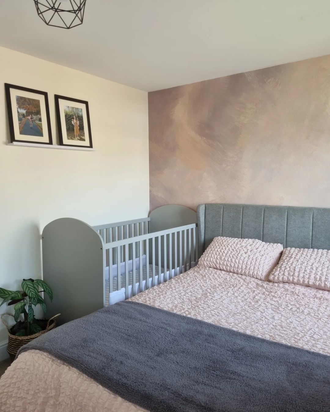 Bedroom with gray crib next to bed with pink bedding and gray throw blanket. Two framed photos on wall.