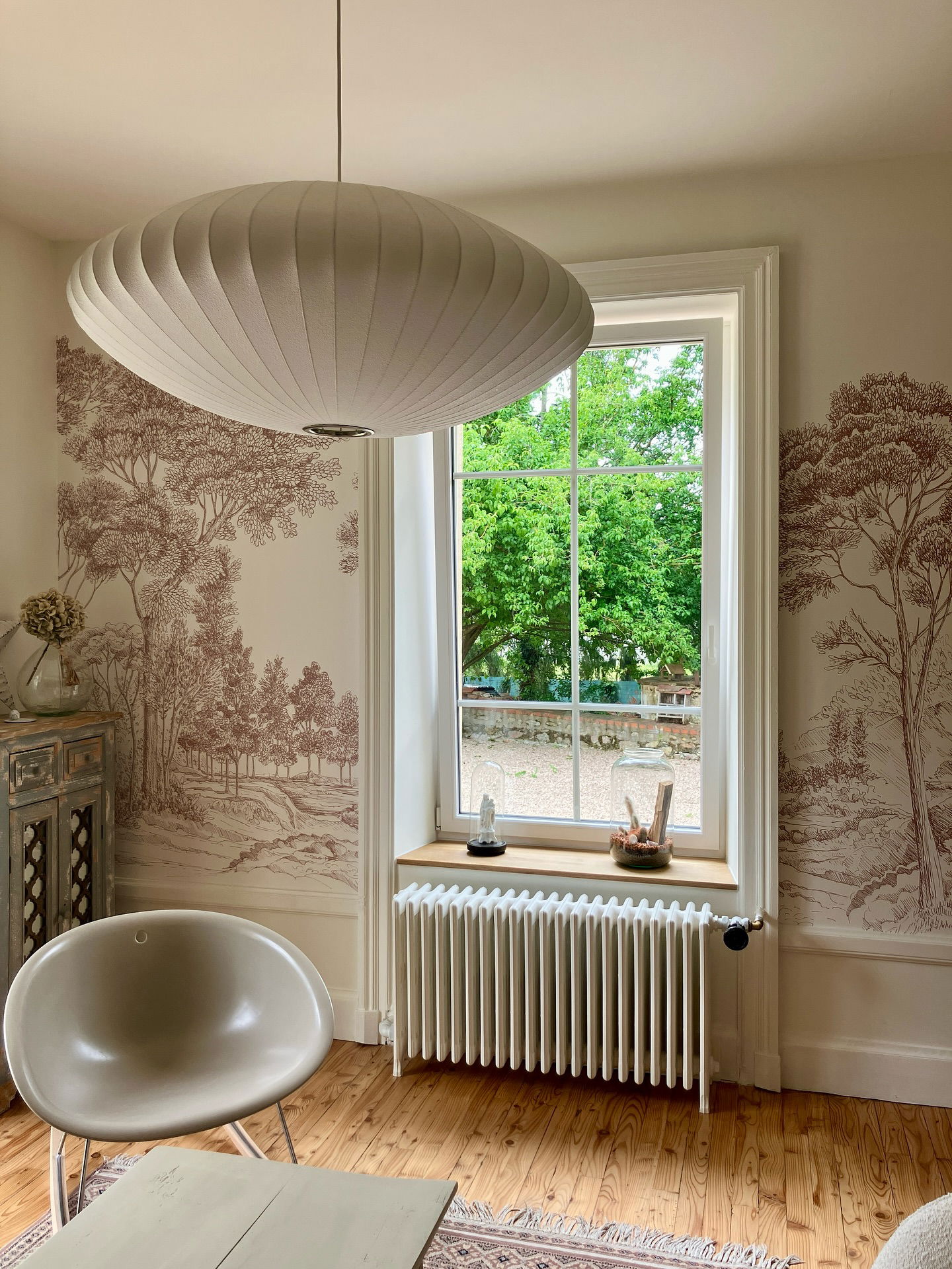 Living room with Nelson Bubble Lamp, tree-themed wallpaper, and window view.