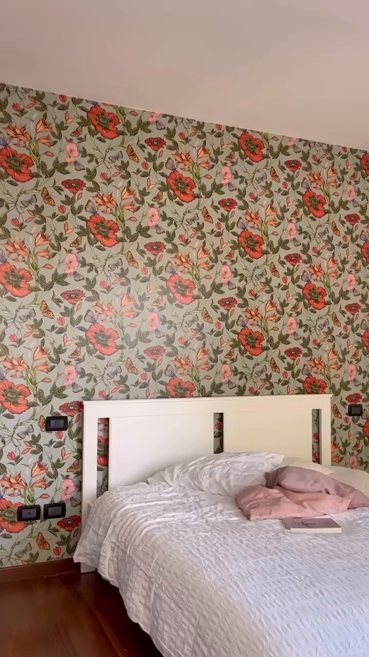 Bedroom with white bed, floral wallpaper, and pink blanket.