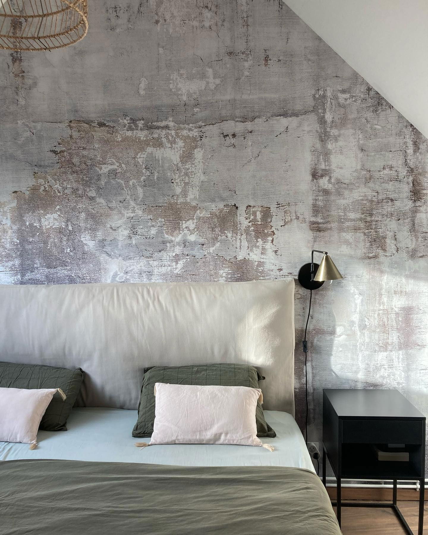 Slaapkamer met muur met textuur, wit hoofdeinde en zwart nachtkastje. Bed heeft groene en roze kussens.