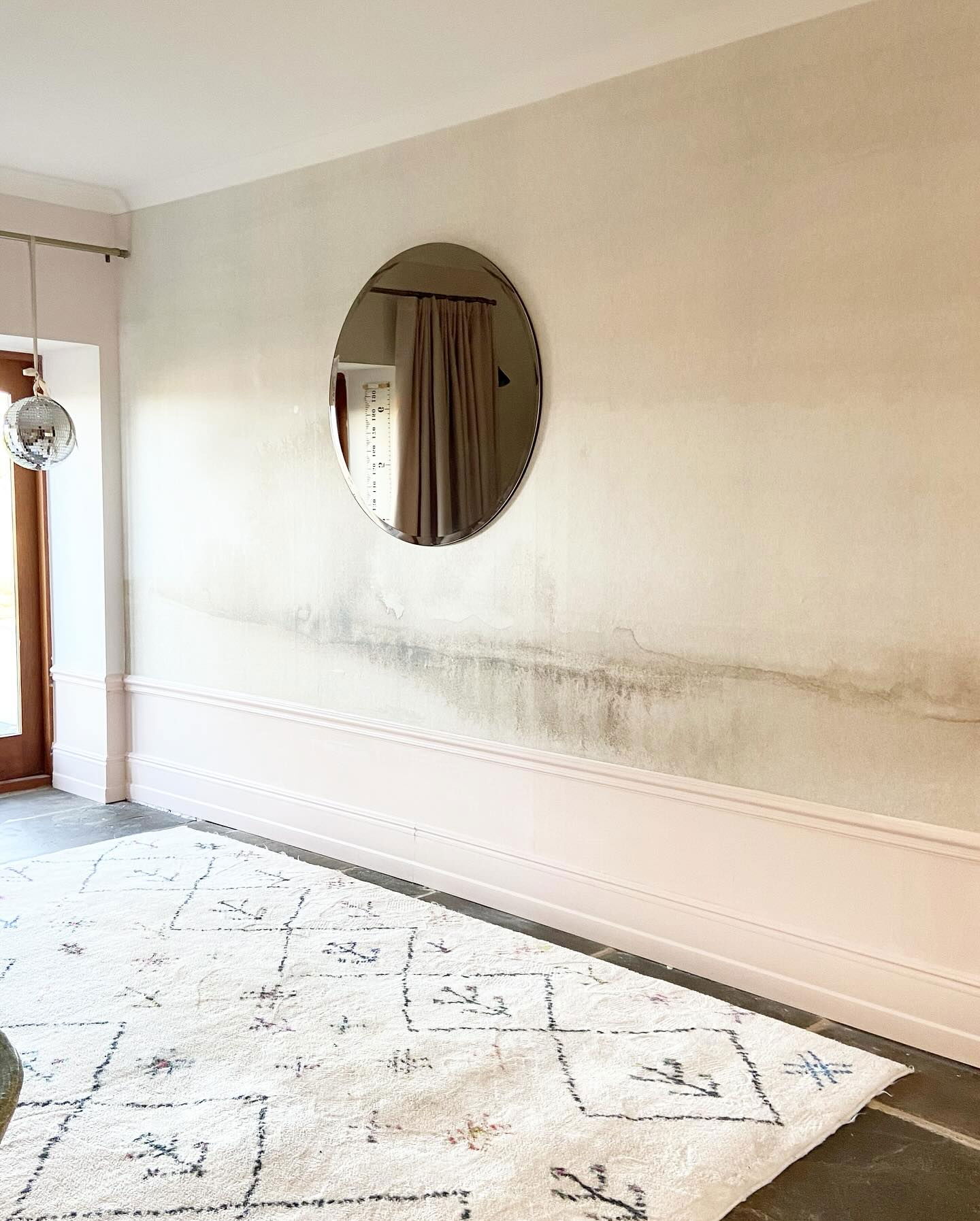 Interior view with round mirror on textured wall, pink trim, and patterned white rug.
