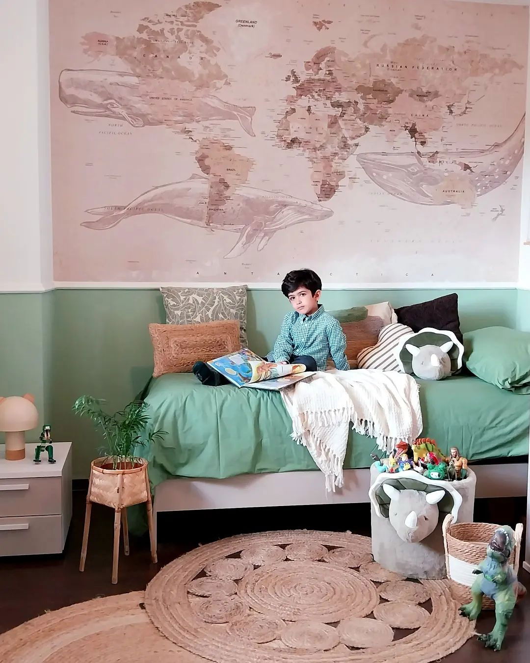 Boy reading on a green bed in a room with a world map mural and dinosaur decor.