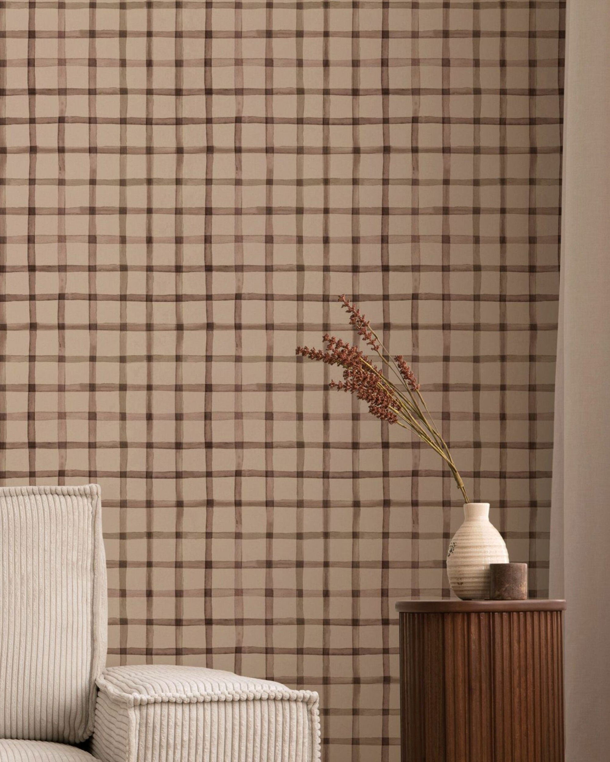 Beige behang met een bruin ruitpatroon, een vaas met gedroogde bloemen en een corduroy stoel.