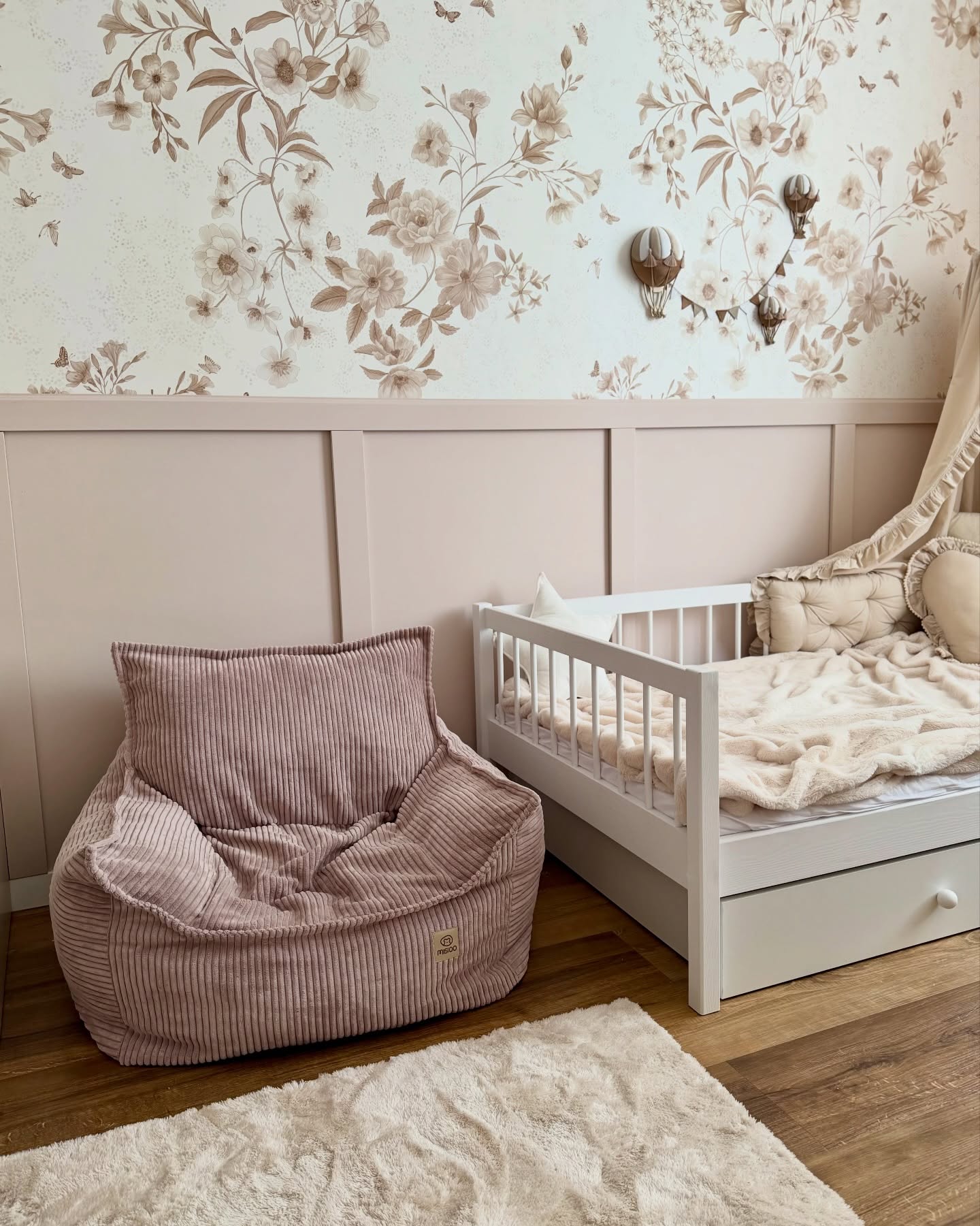 Pink corduroy beanbag chair next to a white crib with a floral wallpaper background.