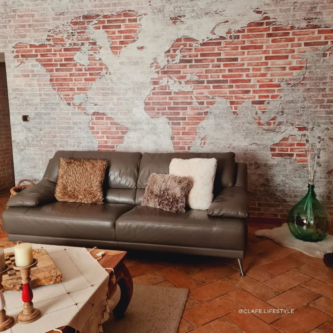 Living room with brown leather sofa, decorative pillows, and world map brick wall.