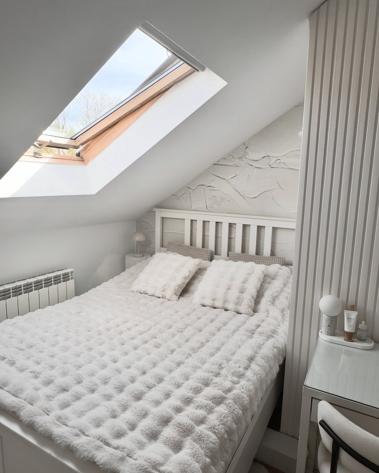 Dachbodenschlafzimmer mit weißem Bett, strukturierter Decke und Dachfenster.