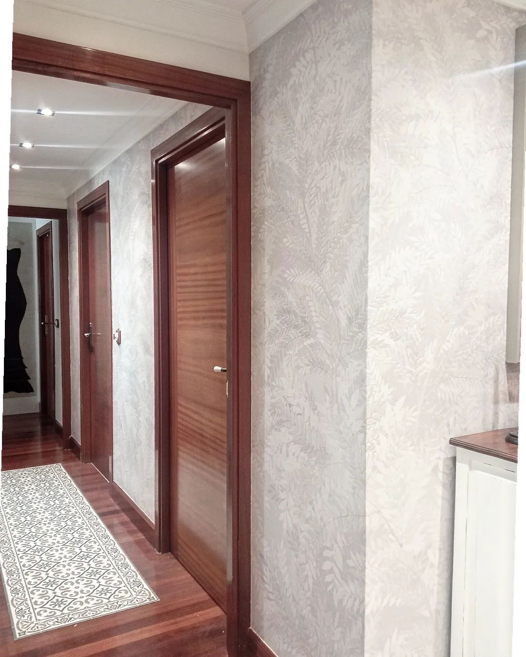 Hallway with wood doors and floors, patterned rug, and leaf-patterned wallpaper.