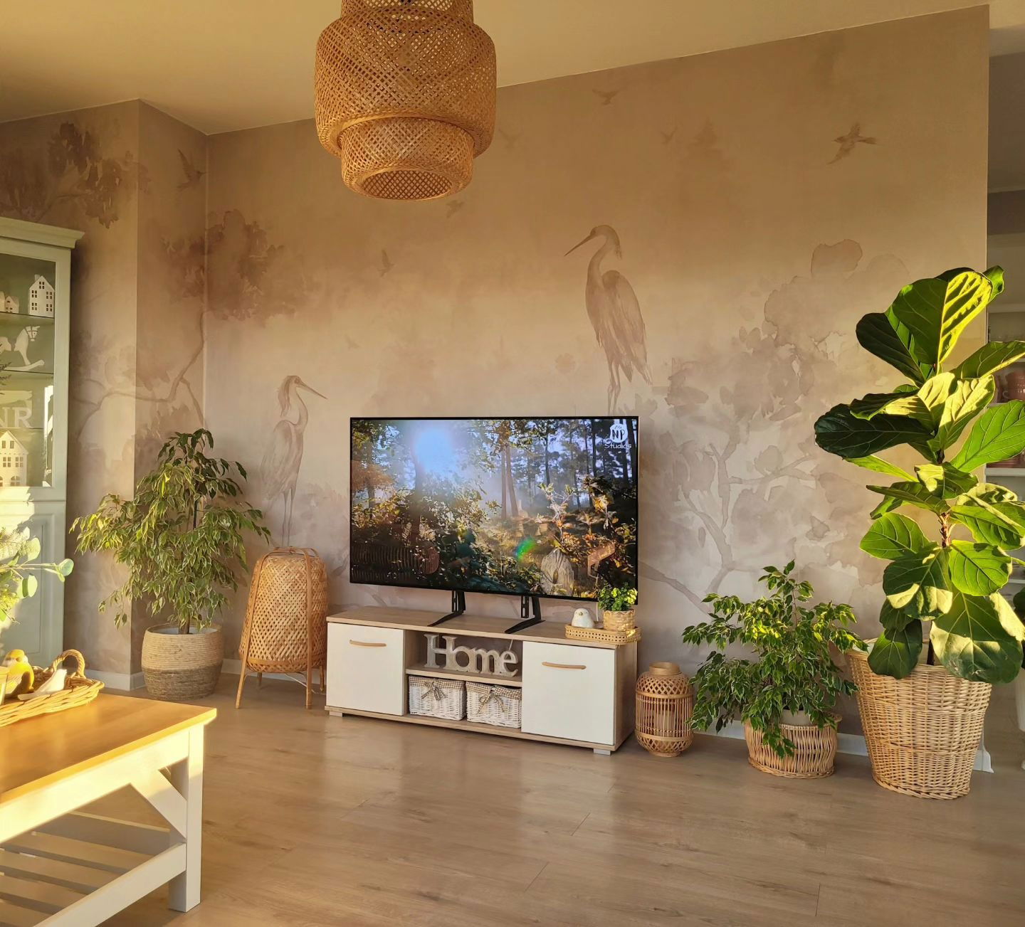 Living room with heron wallpaper, TV on white cabinet, and woven pendant light.