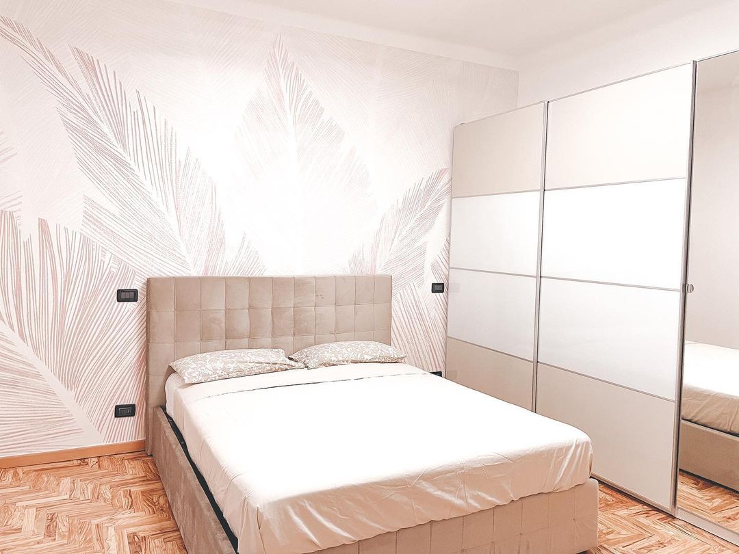 Bedroom with beige bed, leaf-patterned wallpaper, and white closet with mirrored door.