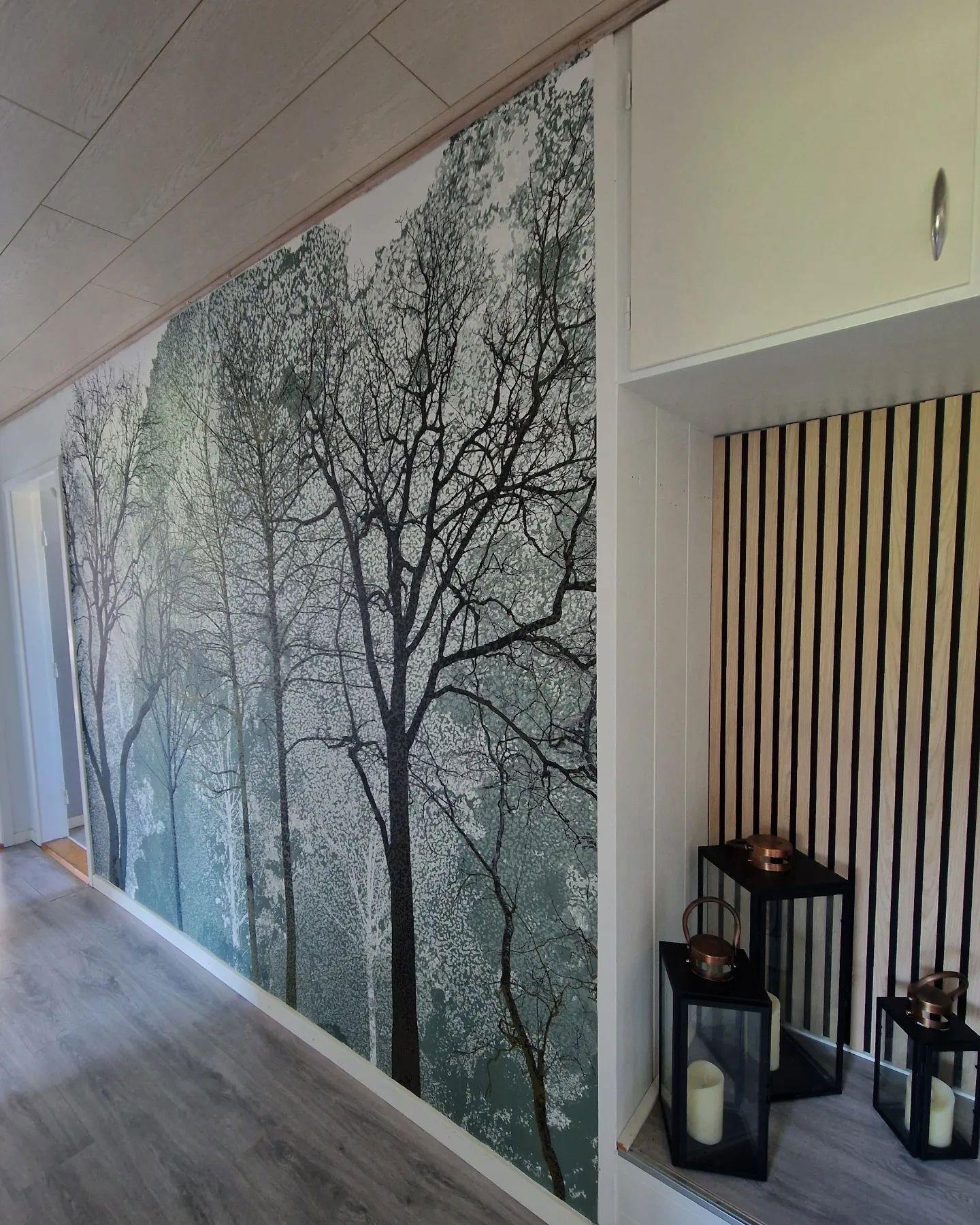 Couloir avec papier peint d'arbre, mur d'accent en lattes de bois et lanternes à bougies noires.