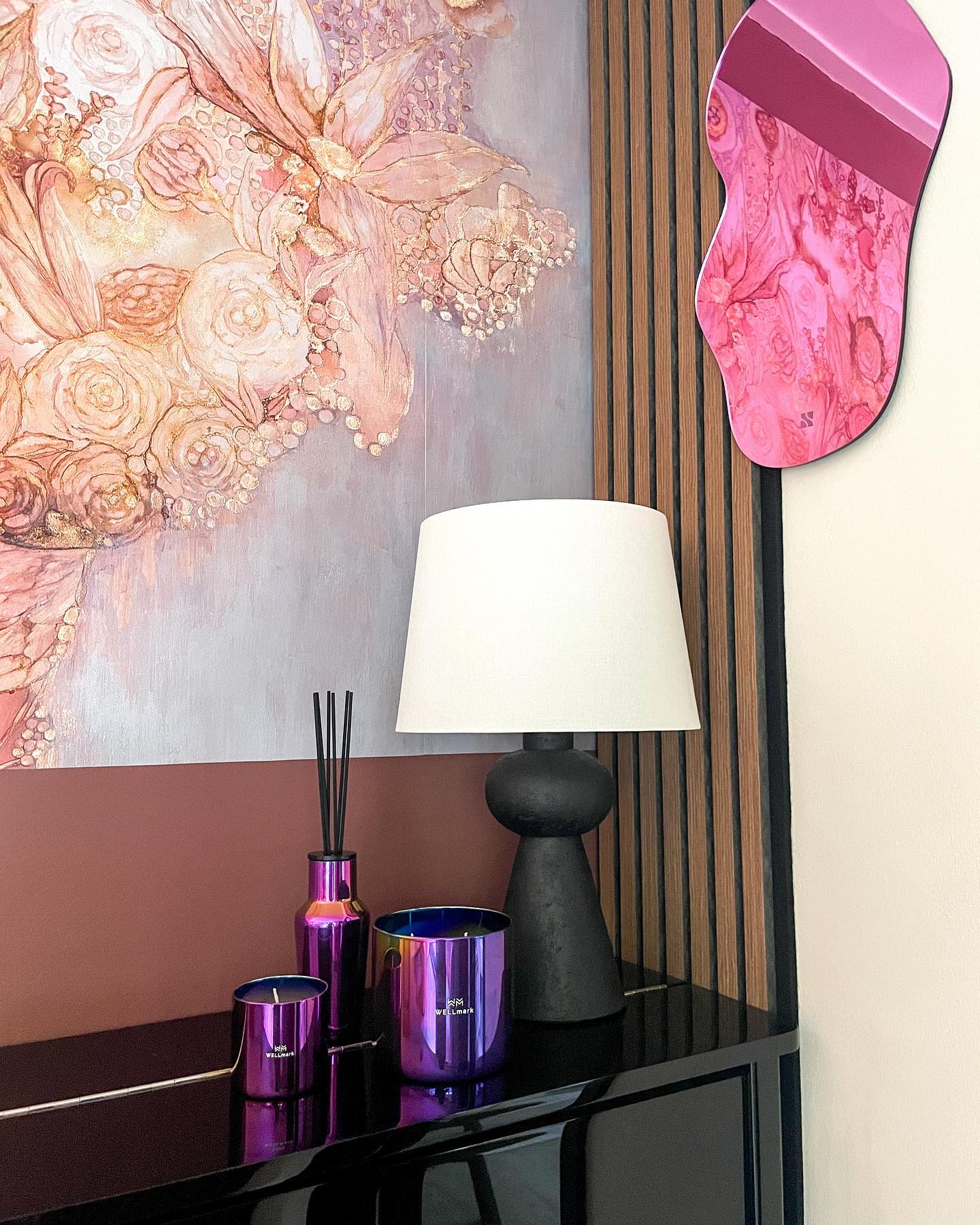 Interiørdekor med blomsterkunst, rosa speil, svart lampe og lilla lys.