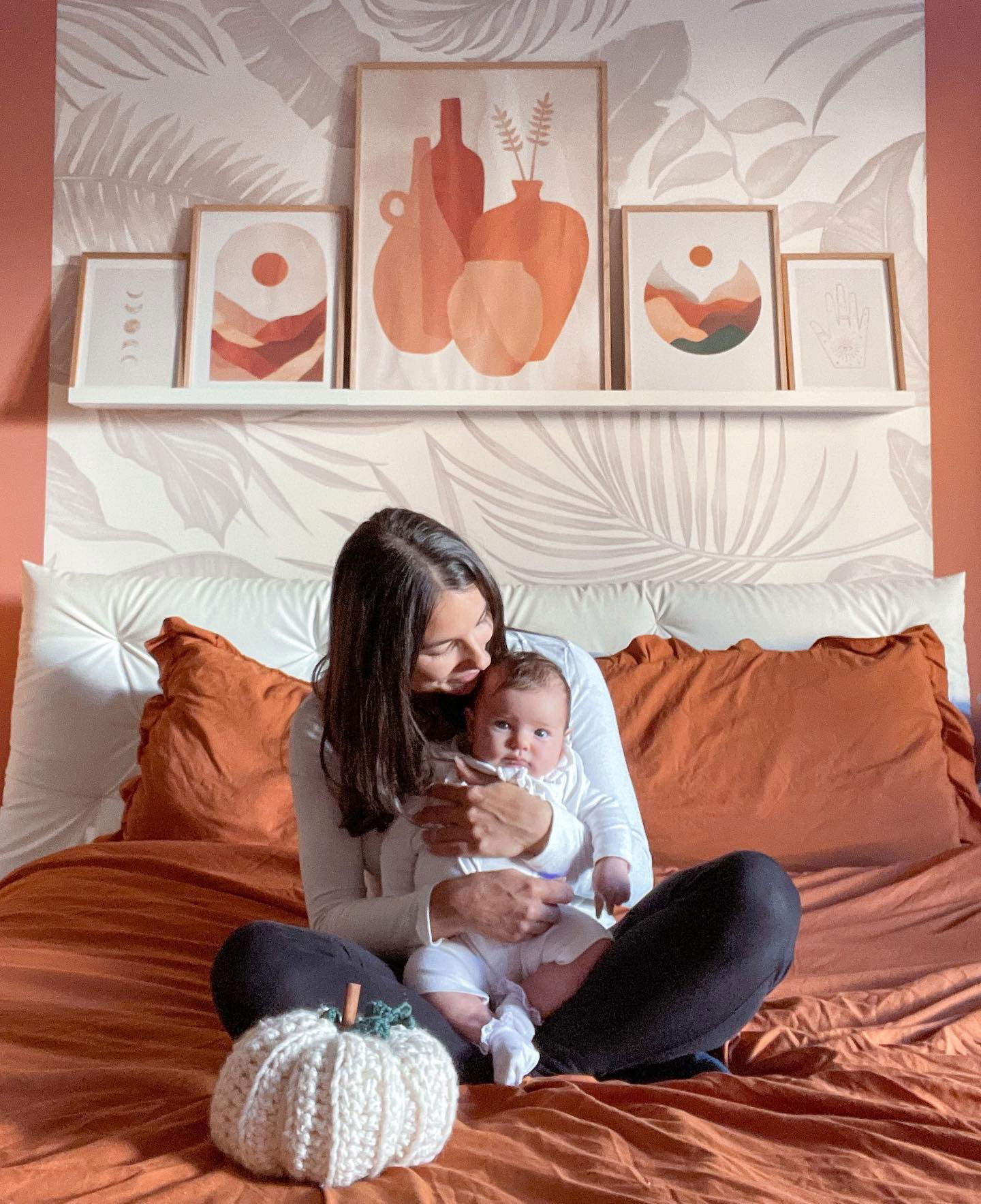 Una donna che tiene in braccio un bambino su un letto arancione con una zucca lavorata a maglia.
