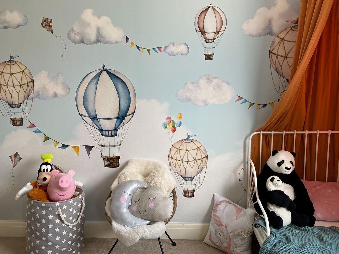 Chambre d'enfant avec papier peint de montgolfière, animaux en peluche et coussins lune et nuage.